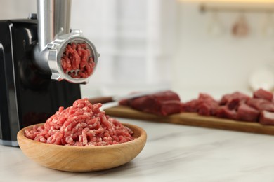 Photo of Electric meat grinder with minced beef on white marble table in kitchen, space for text