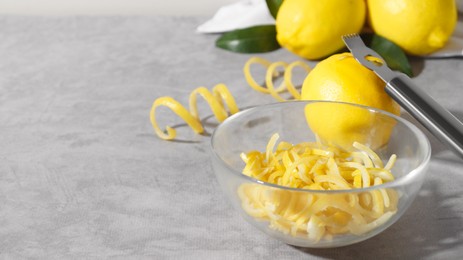 Photo of Bowl with peel pieces, fresh lemons and zester on grey table, space for text