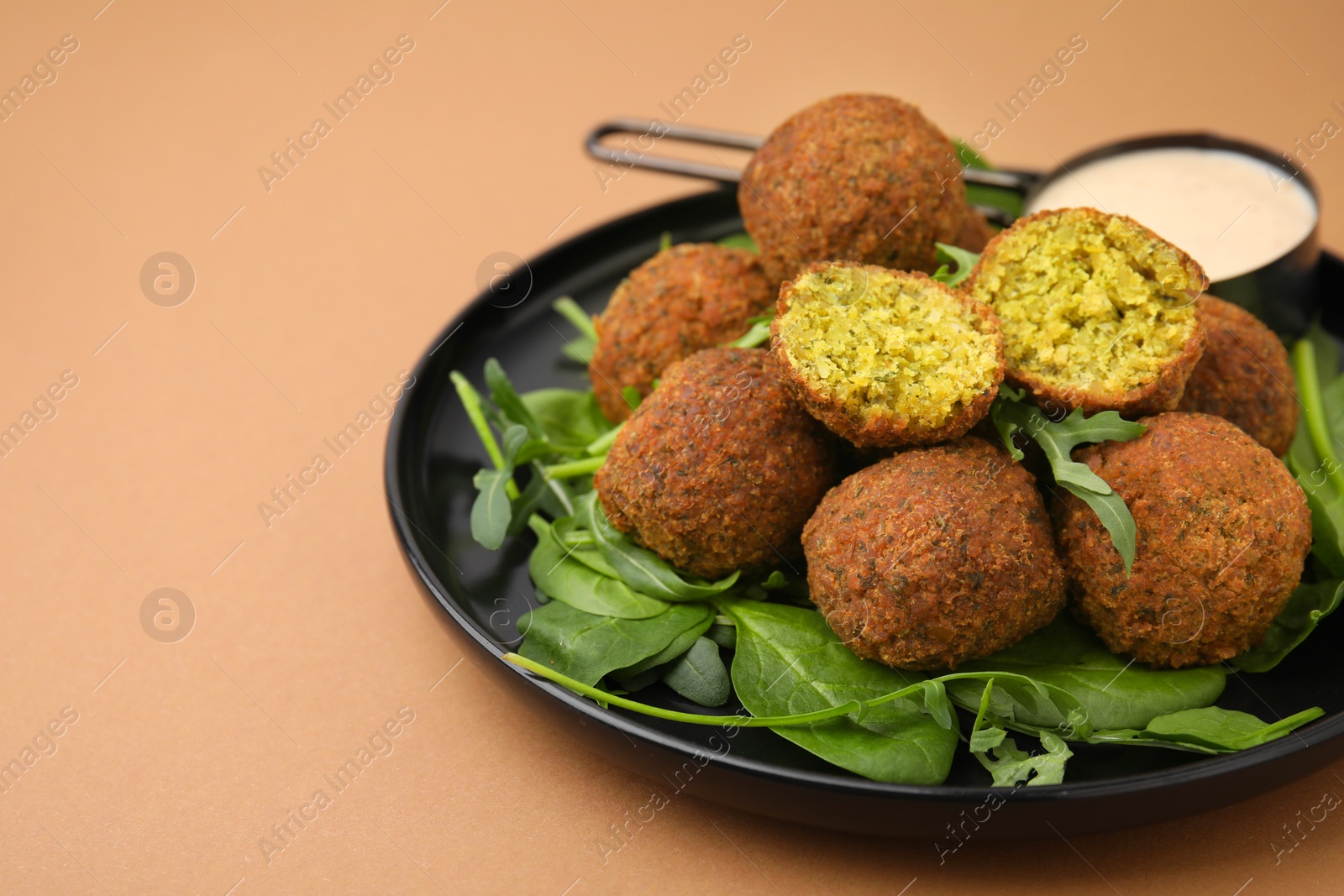 Photo of Delicious falafel balls, herbs and sauce on pale brown, space for text