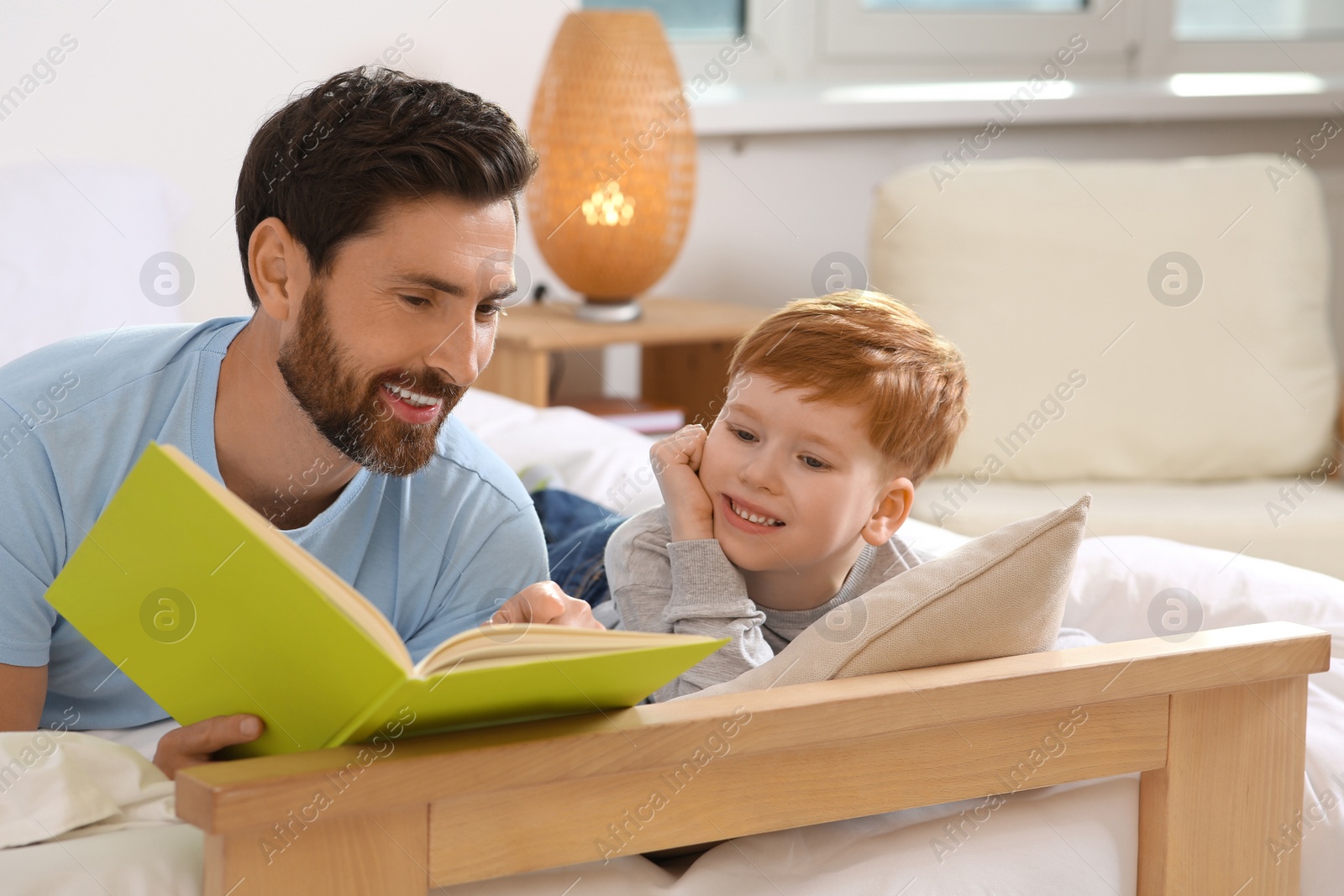 Photo of Father reading book with his child on bed at home