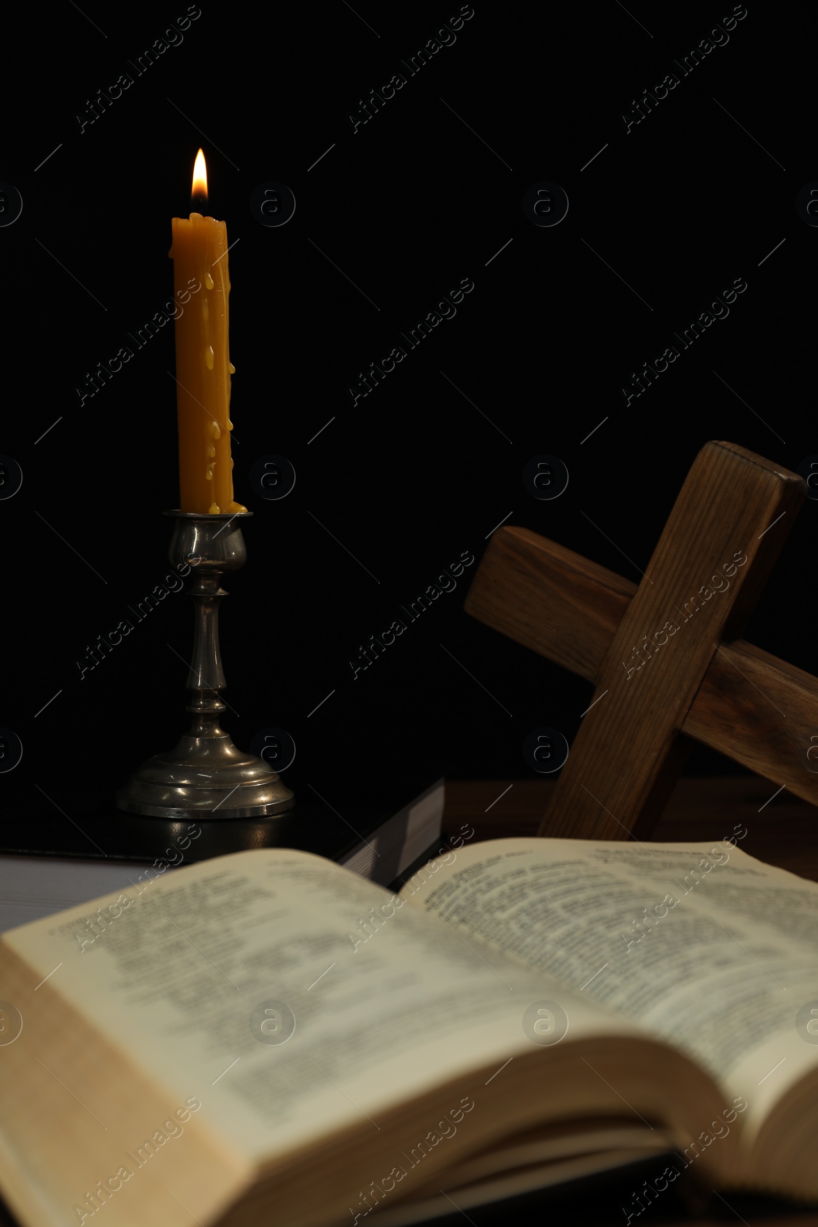 Photo of Church candle, Bible and cross on table against black background