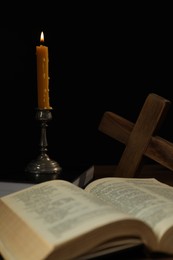 Photo of Church candle, Bible and cross on table against black background