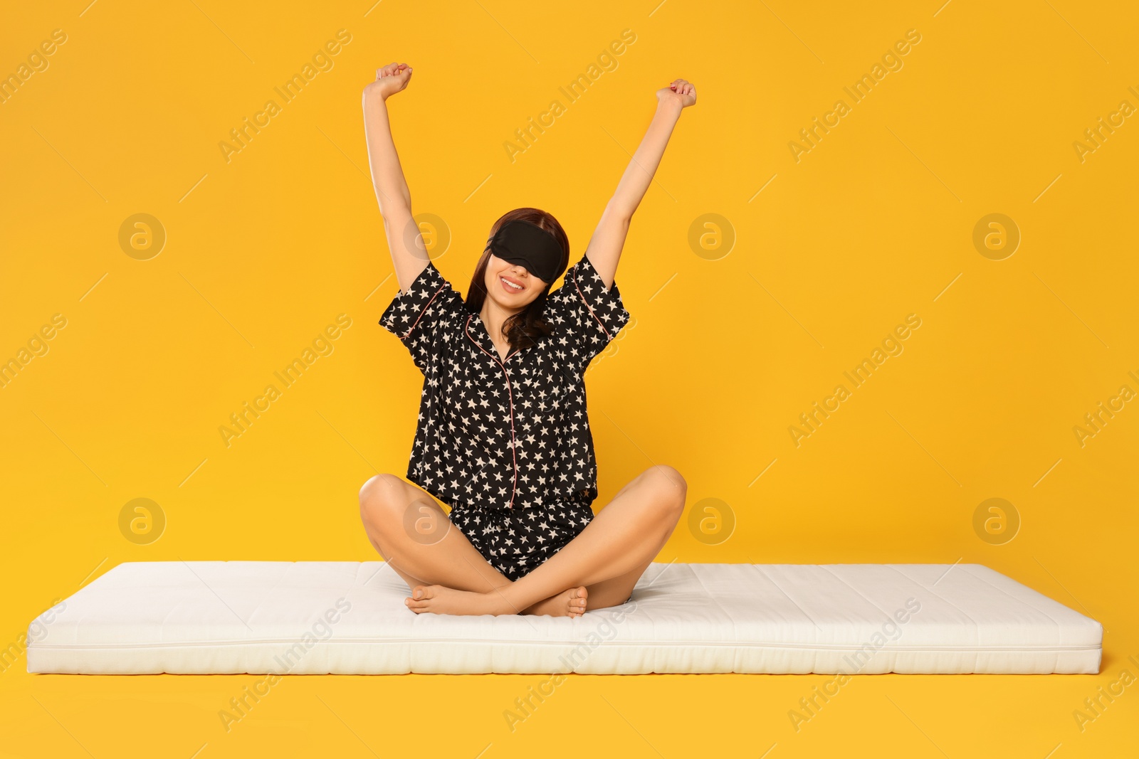 Photo of Woman in sleep mask stretching on soft mattress against orange background