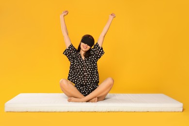 Photo of Woman in sleep mask stretching on soft mattress against orange background