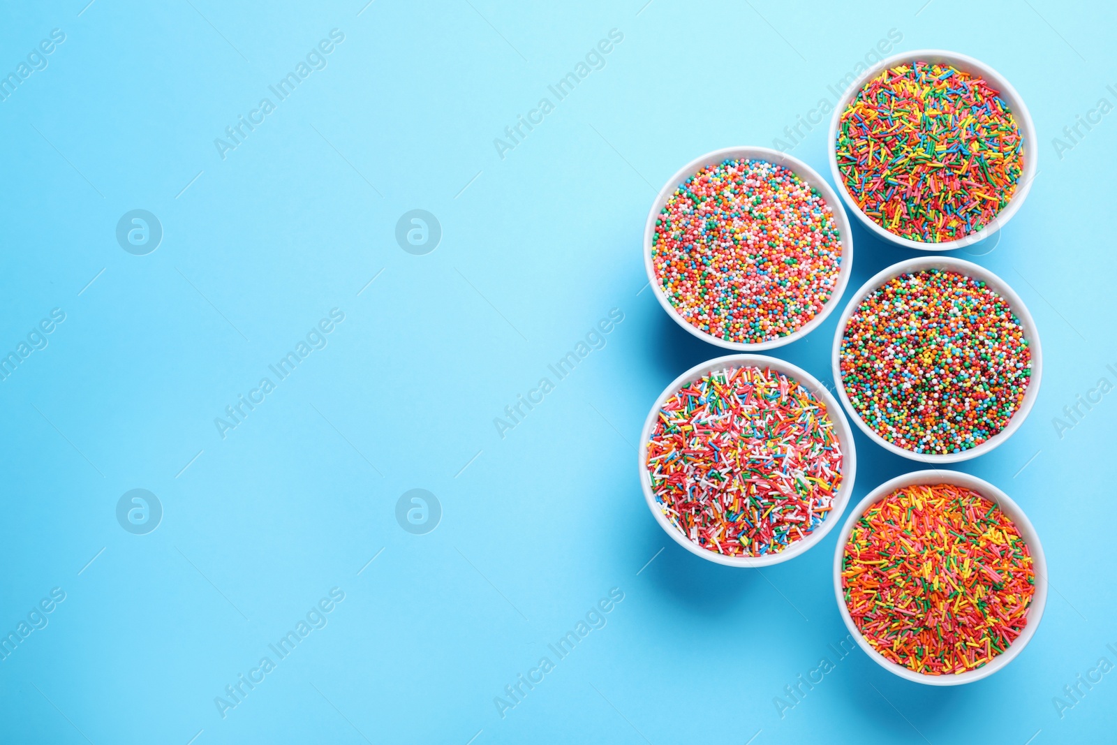 Photo of Colorful sprinkles in bowls on light blue background, flat lay with space for text. Confectionery decor