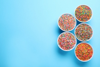 Photo of Colorful sprinkles in bowls on light blue background, flat lay with space for text. Confectionery decor
