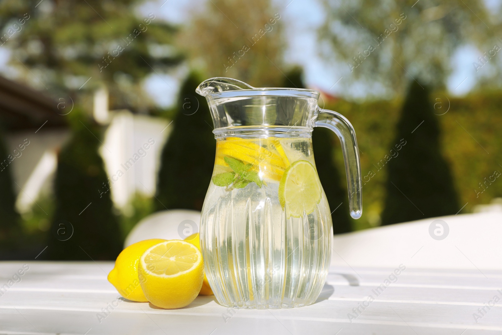 Photo of Jug of water with lemons and mint on white wooden table outdoors