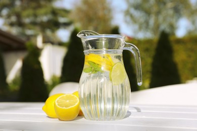 Jug of water with lemons and mint on white wooden table outdoors