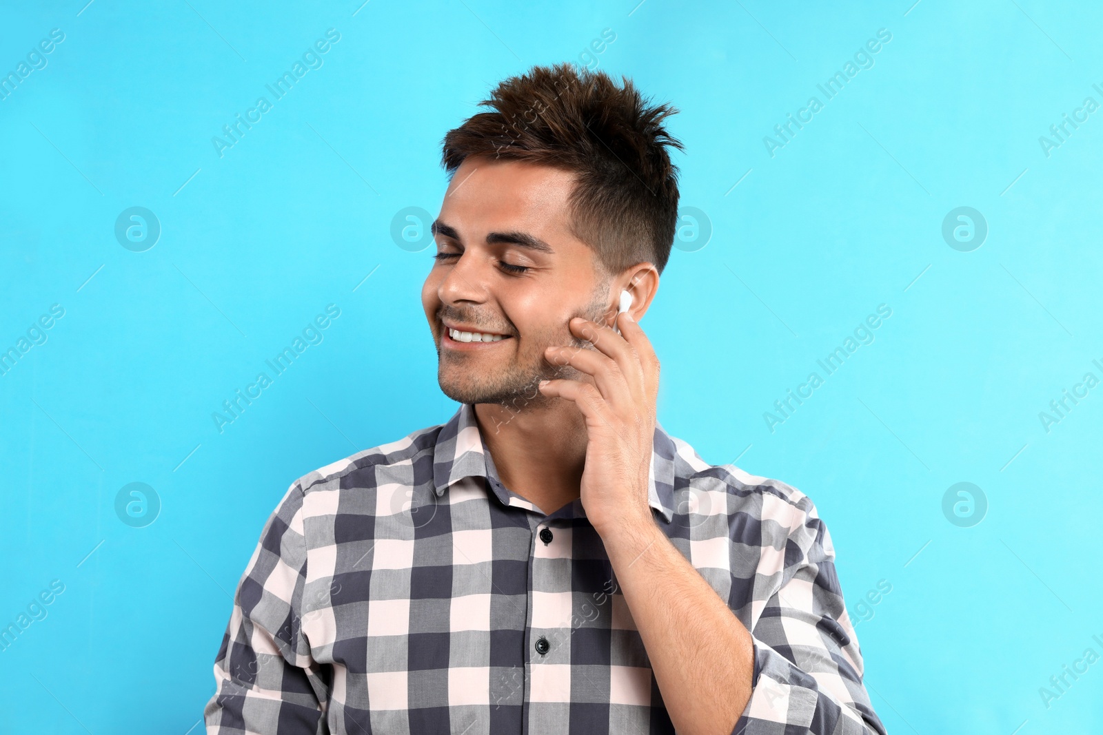 Photo of Happy young man listening to music through wireless earphones on light blue background