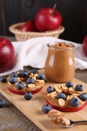 Photo of Slices of fresh apple with peanut butter and blueberries on wooden table, closeup