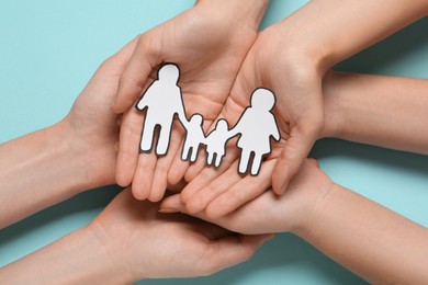 People holding paper family cutout on light blue background, top view