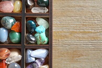 Box with different beautiful gemstones on wooden table, flat lay. Space for text