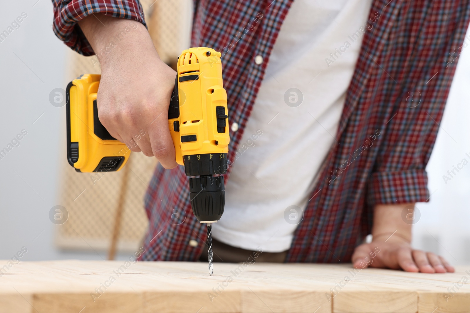 Photo of Young handyman working with electric drill at table in workshop, closeup