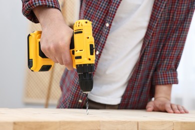 Photo of Young handyman working with electric drill at table in workshop, closeup