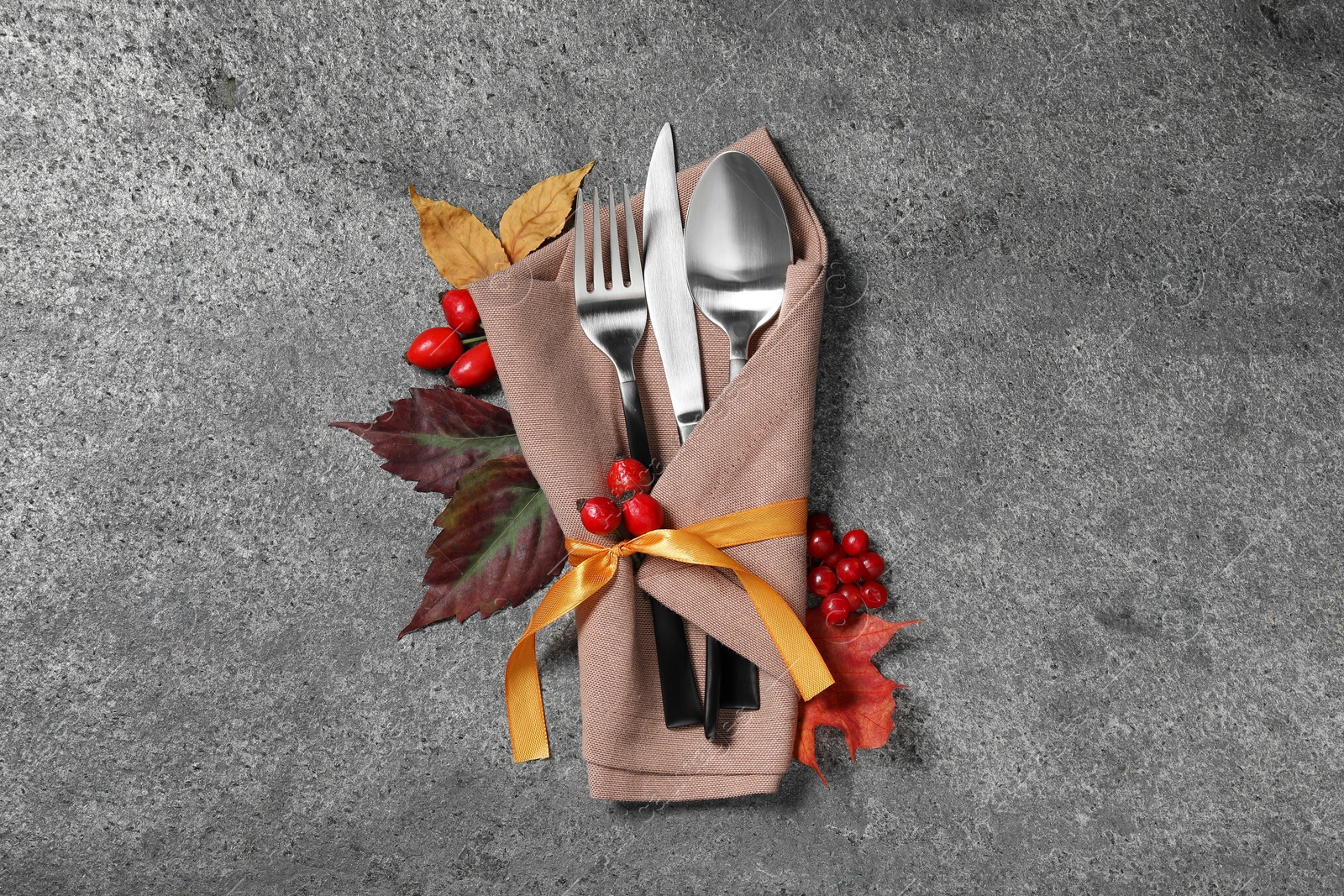 Photo of Thanksgiving table setting. Cutlery, napkin, autumn leaves and berries on grey background, flat lay