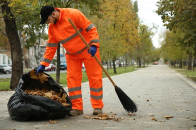 Photo of Worker cleaning street from fallen leaves on autumn day