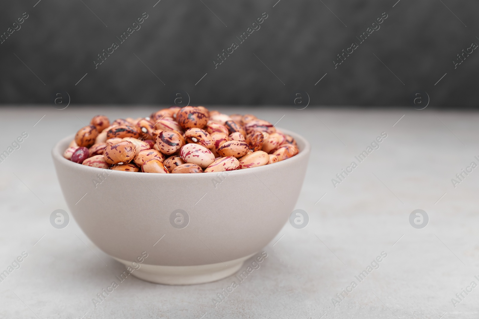 Photo of Bowl with dry kidney beans on light grey table, closeup. Space for text