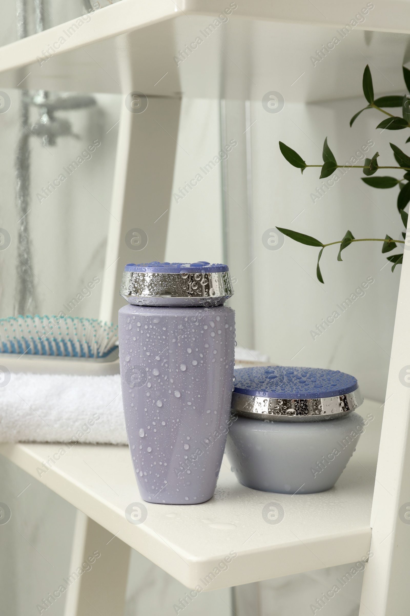 Photo of Hair care cosmetic products, towel and brush on white shelf indoors