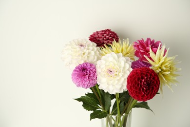 Photo of Bouquet of beautiful Dahlia flowers in vase near white wall. Space for text