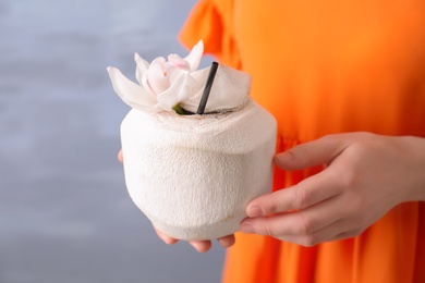 Photo of Woman with fresh coconut drink in nut on color background, closeup