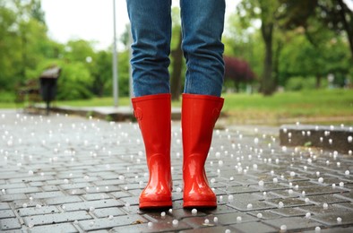 Image of Woman wearing red rubber boots outdoors after thunderstorm with hail, closeup 
