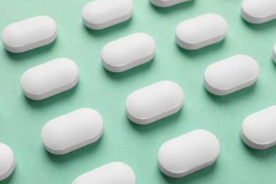 Many white pills on green background, closeup