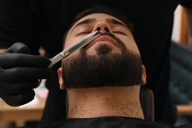 Photo of Professional hairdresser working with mustache of client in barbershop, closeup