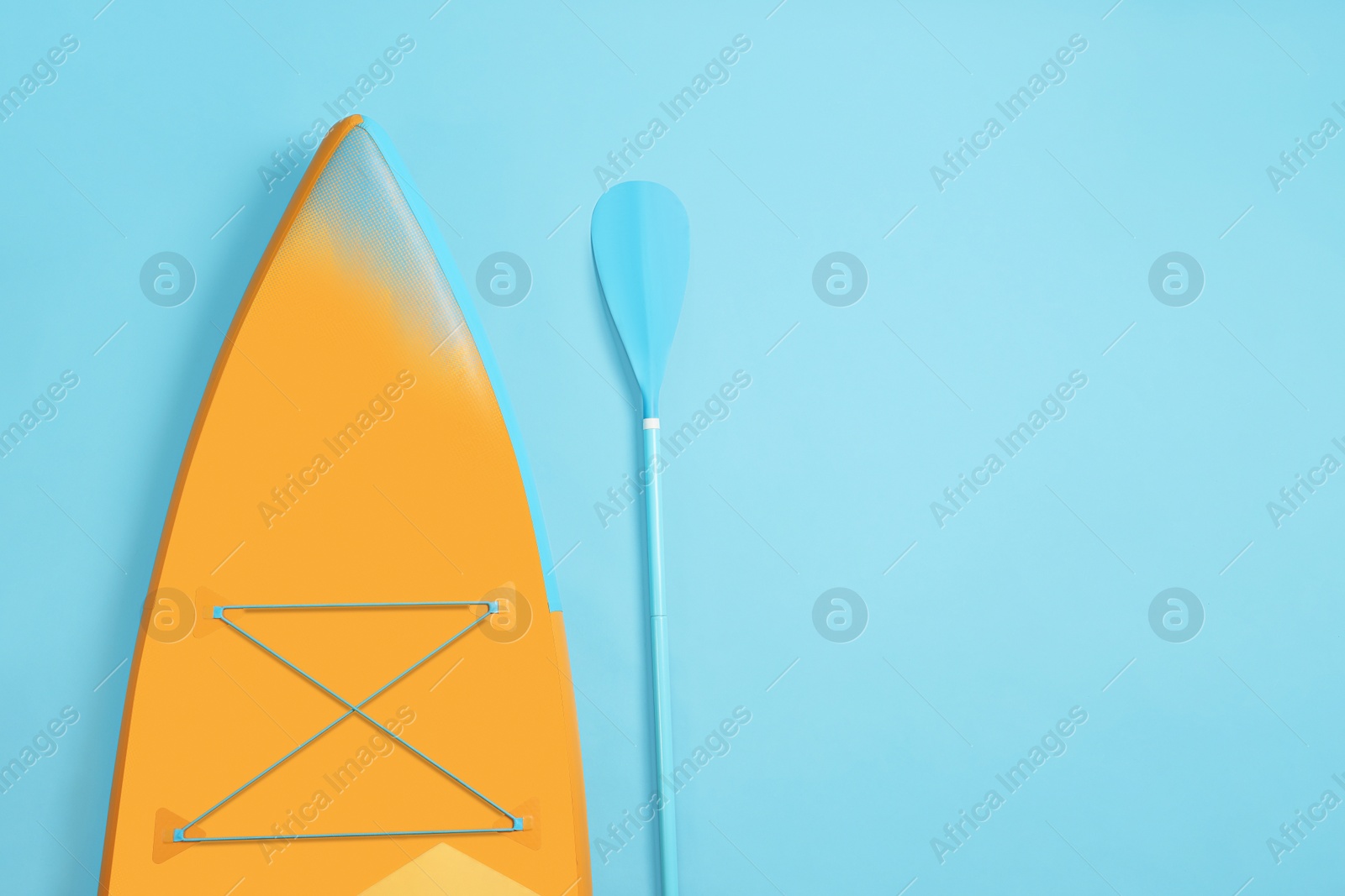 Photo of Board and paddle for standup paddleboarding (SUP) on light blue background, flat lay. Space for text