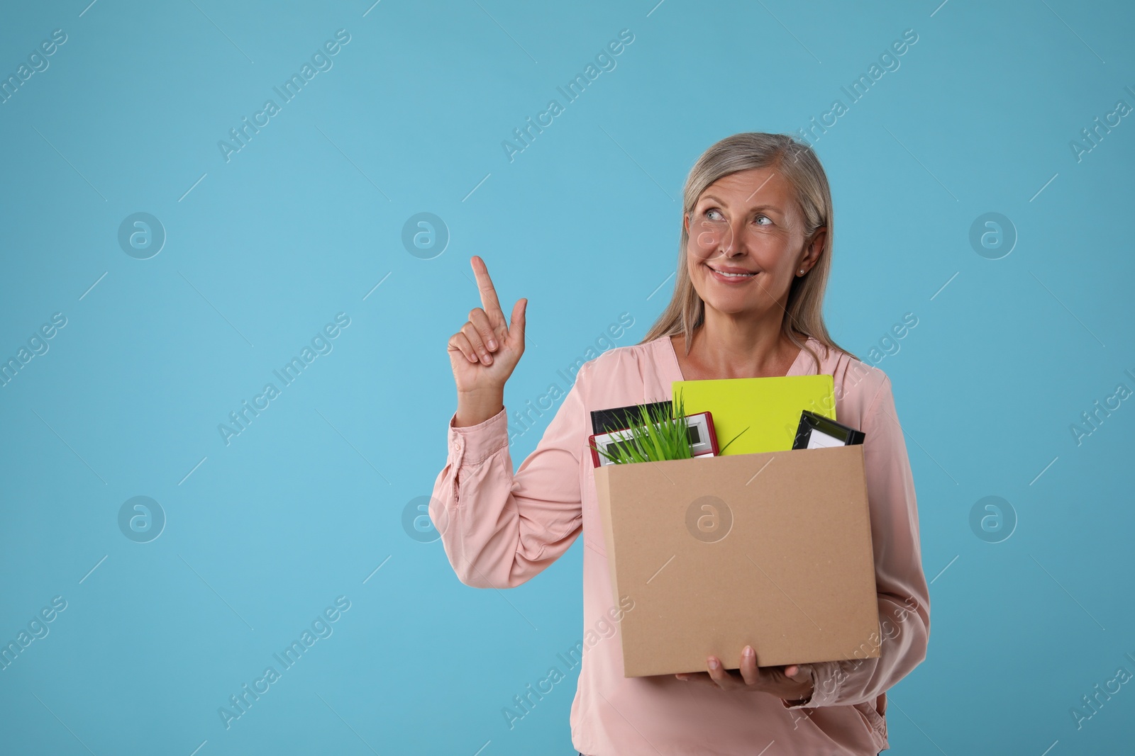 Photo of Happy unemployed senior woman with box of personal office belongings on light blue background. Space for text