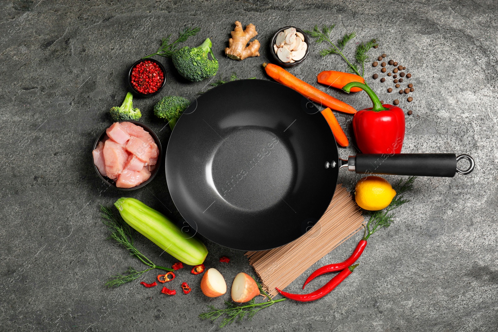 Photo of Empty iron wok surrounded by raw ingredients on grey table, flat lay