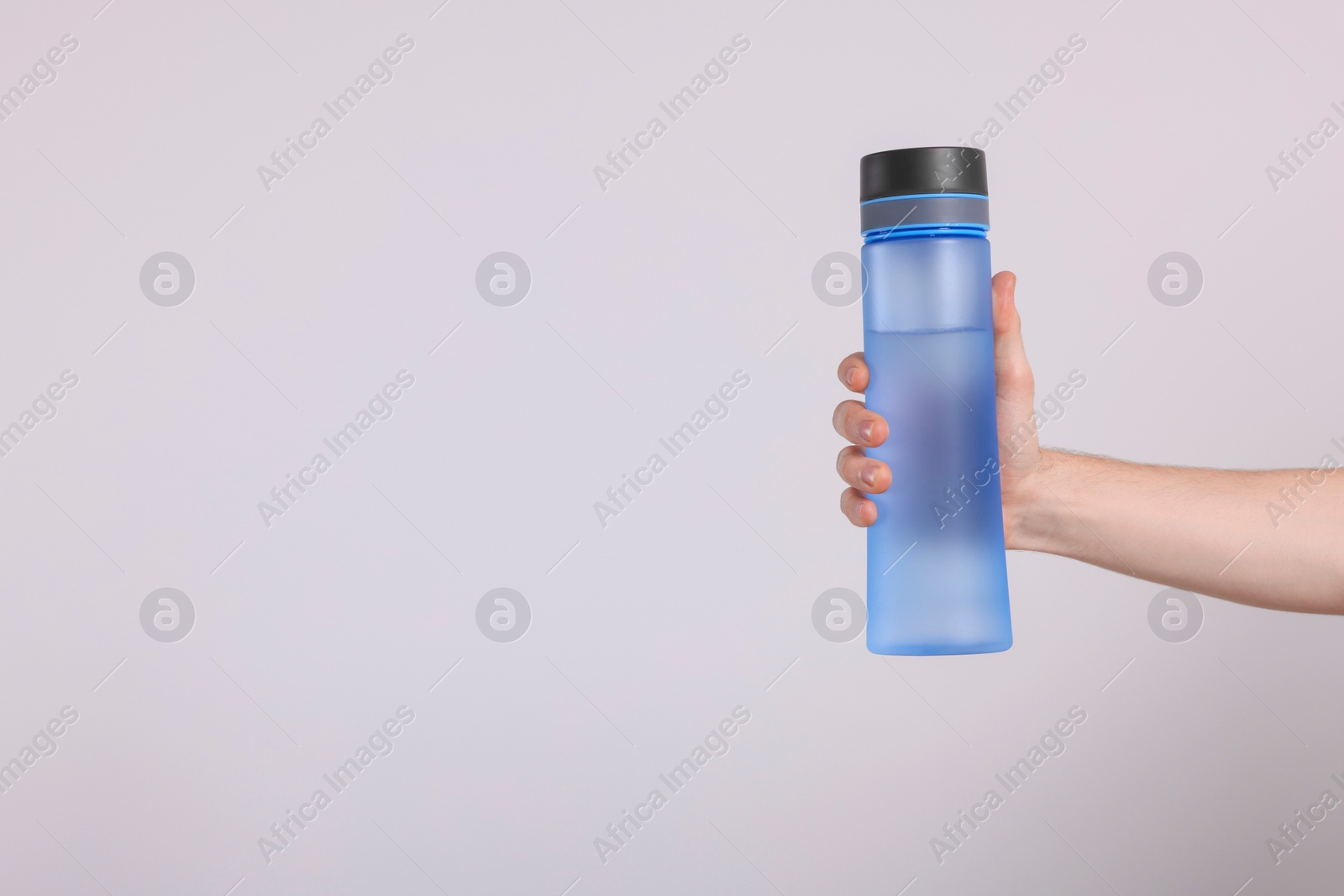 Photo of Man holding transparent plastic bottle with drink on light grey background, closeup. Space for text