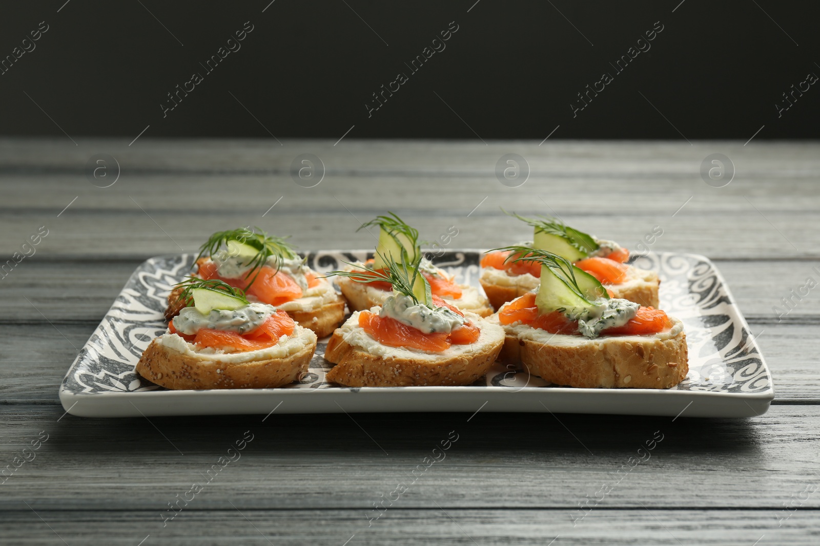 Photo of Tasty canapes with salmon, cucumber, cream cheese and dill on wooden table