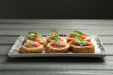 Tasty canapes with salmon, cucumber, cream cheese and dill on wooden table