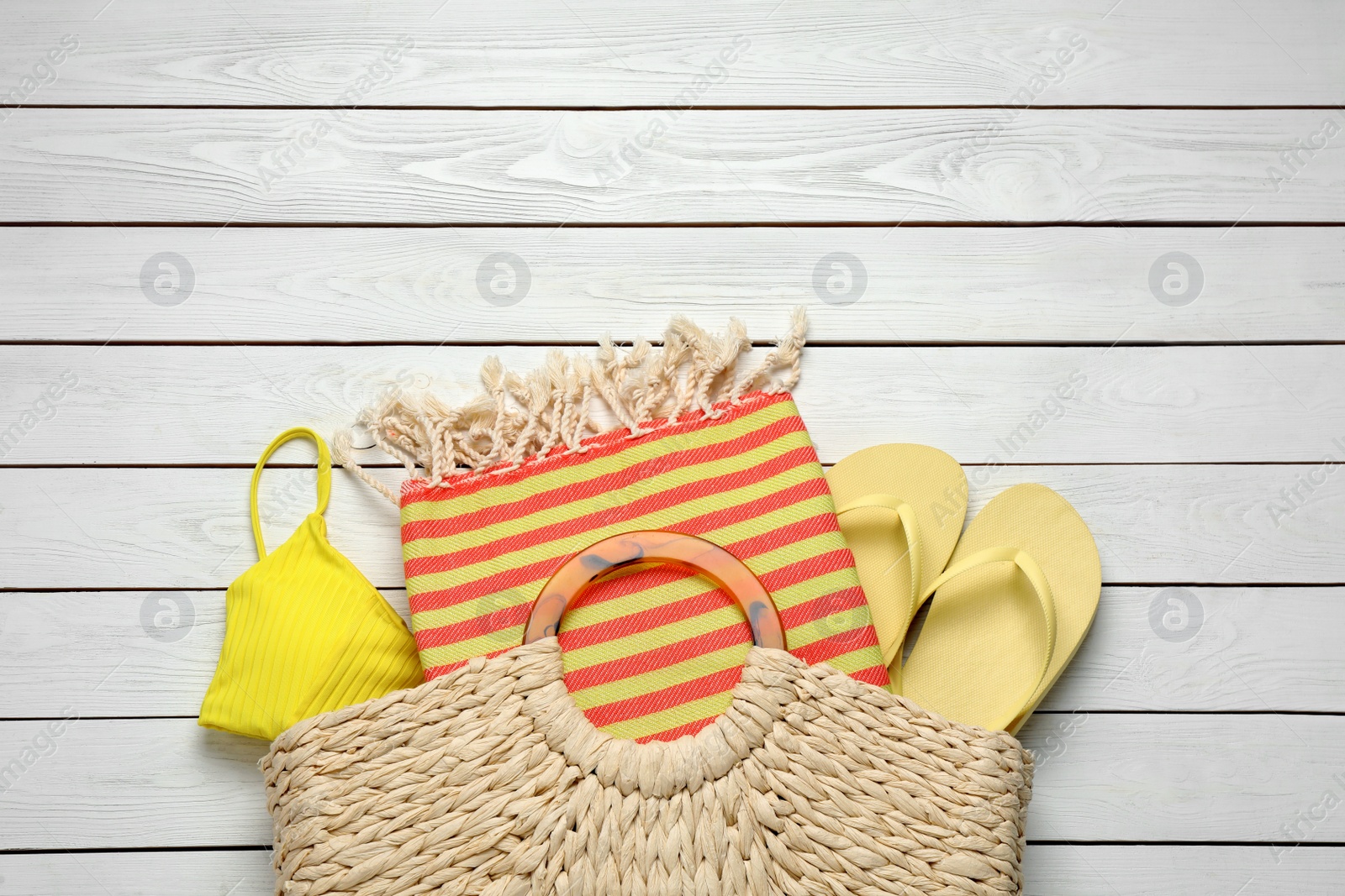 Photo of Beach bag with towel, flip flops and swimsuit on white wooden background, flat lay. Space for text