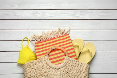 Photo of Beach bag with towel, flip flops and swimsuit on white wooden background, flat lay. Space for text