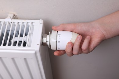 Photo of Girl adjusting heating radiator thermostat near white wall indoors, closeup