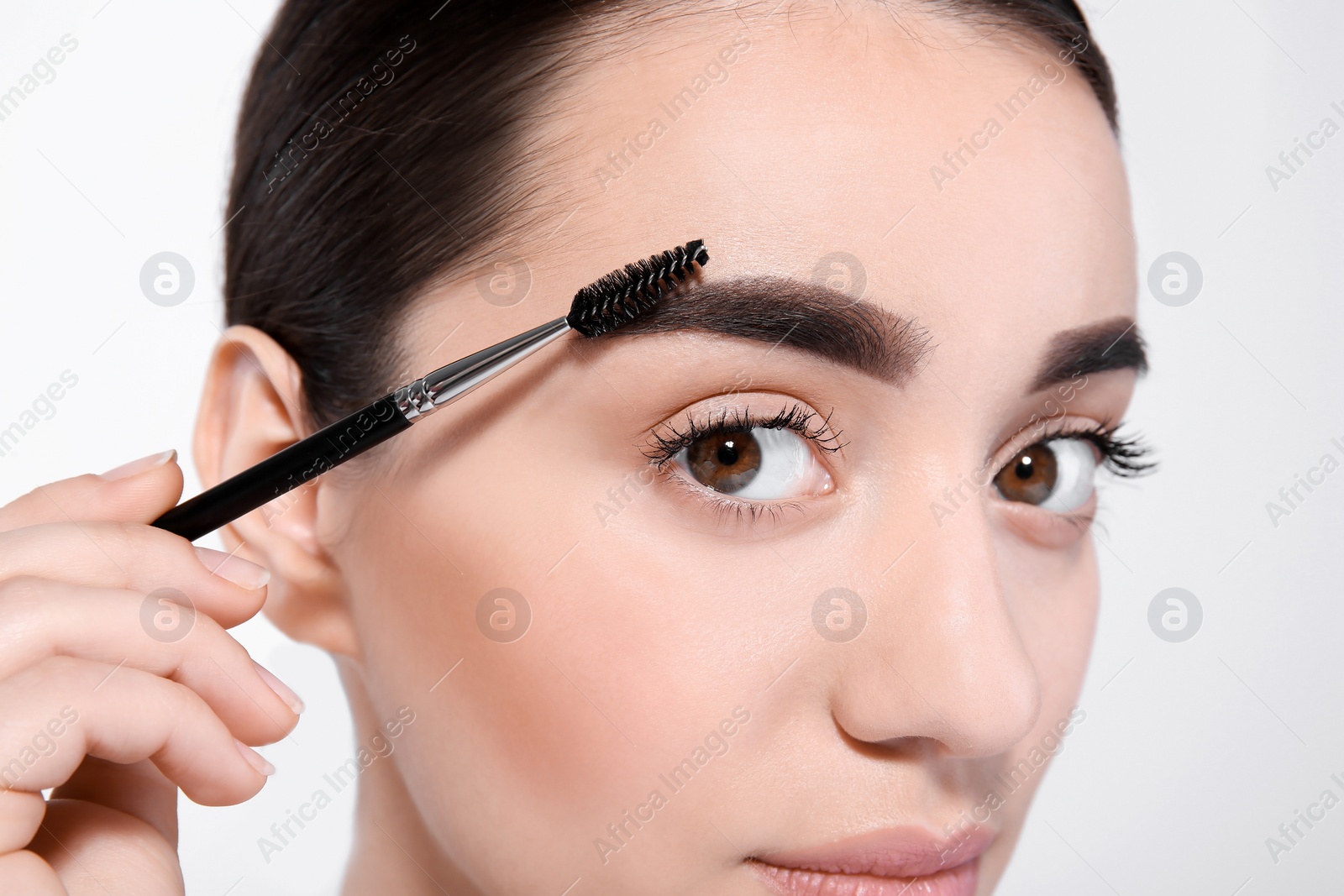 Photo of Beautiful woman with perfect eyebrows applying makeup on light background