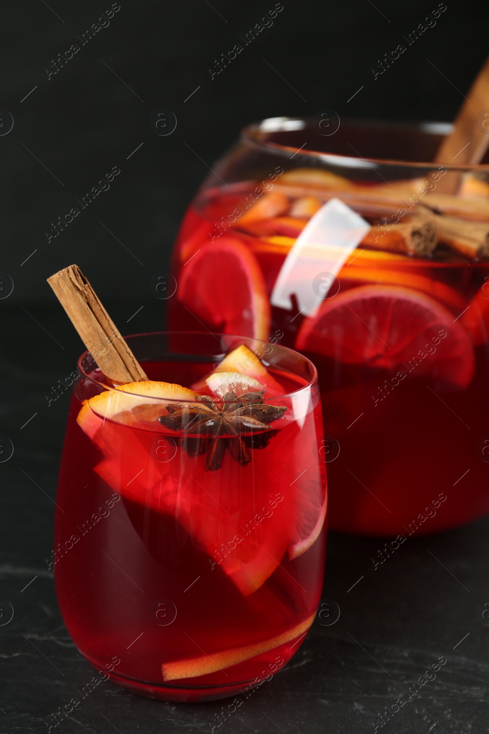 Photo of Glass and bowl of delicious aromatic punch drink on black table