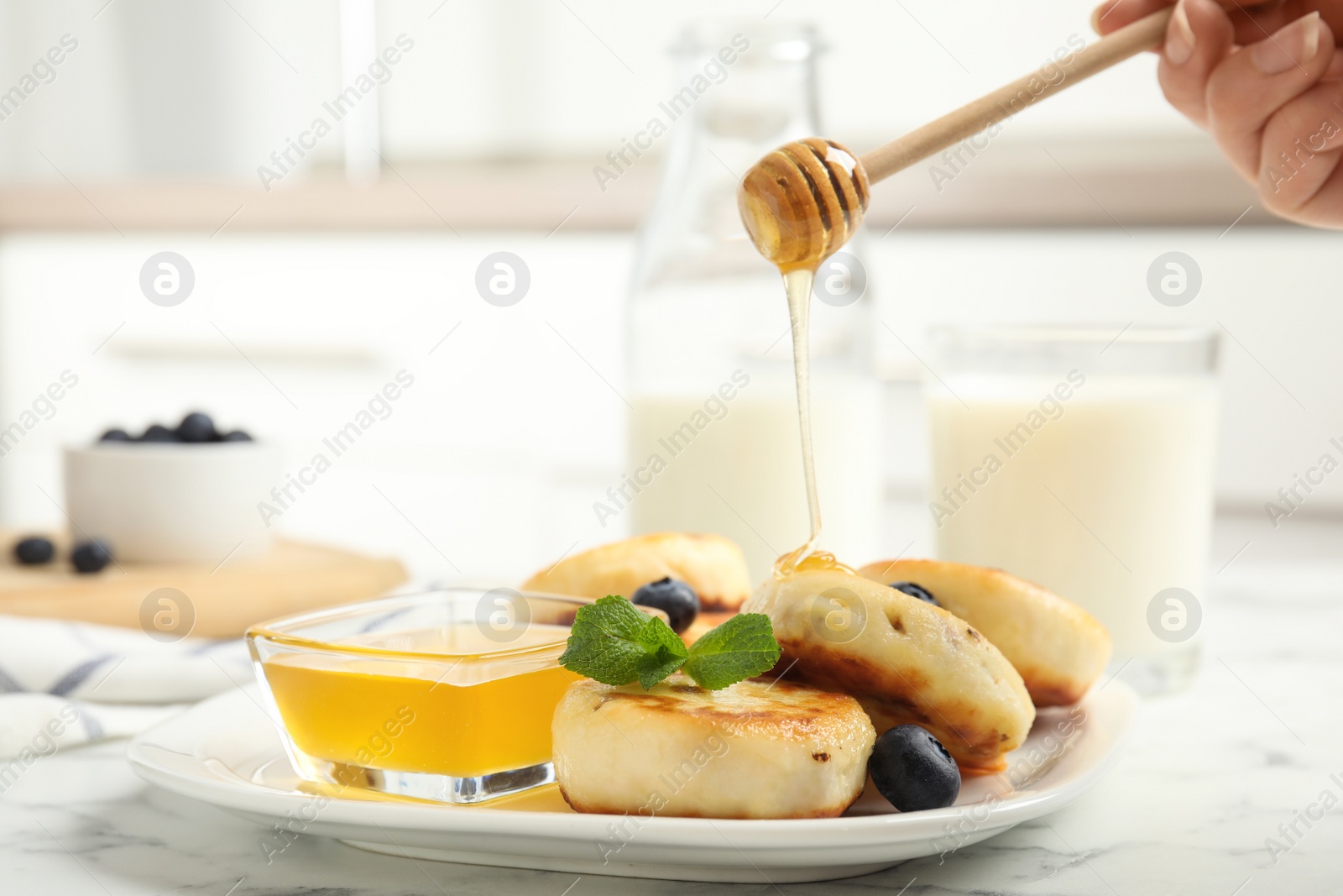 Photo of Woman pouring honey onto delicious cottage cheese on white marble table