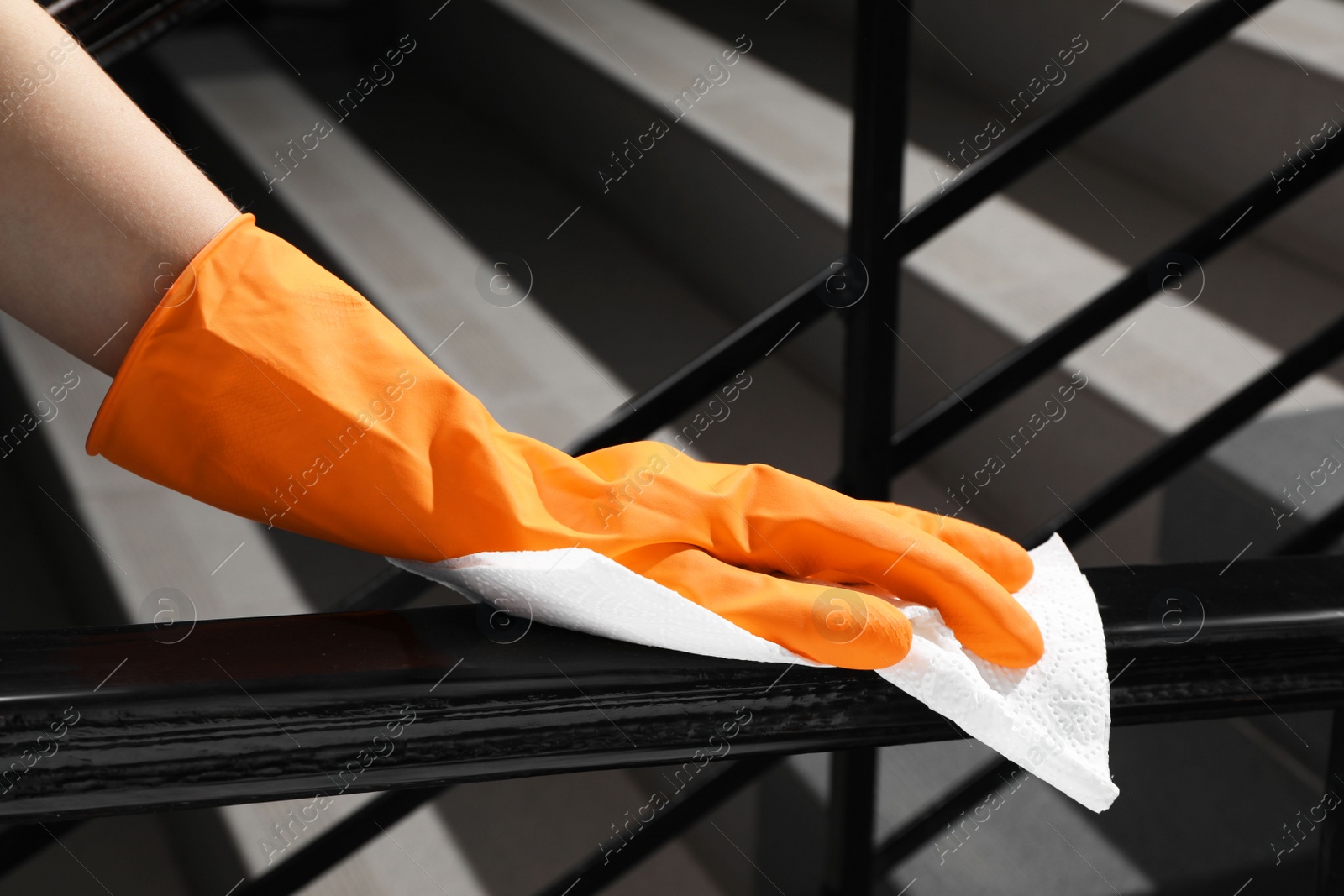 Photo of Woman in glove cleaning railing with paper towel indoors, closeup