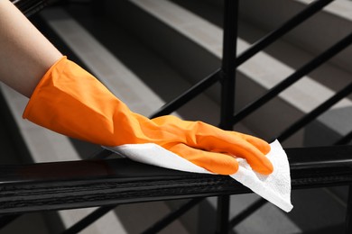 Woman in glove cleaning railing with paper towel indoors, closeup