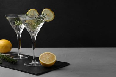 Photo of Martini glasses of refreshing cocktail decorated with lemon slices and rosemary on grey textured table. Space for text