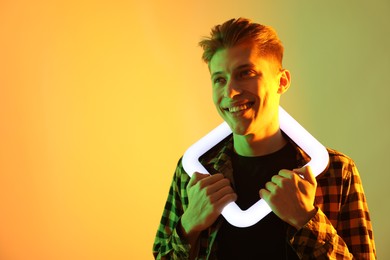 Photo of Young man with square lamp on color background in neon lights. Space for text