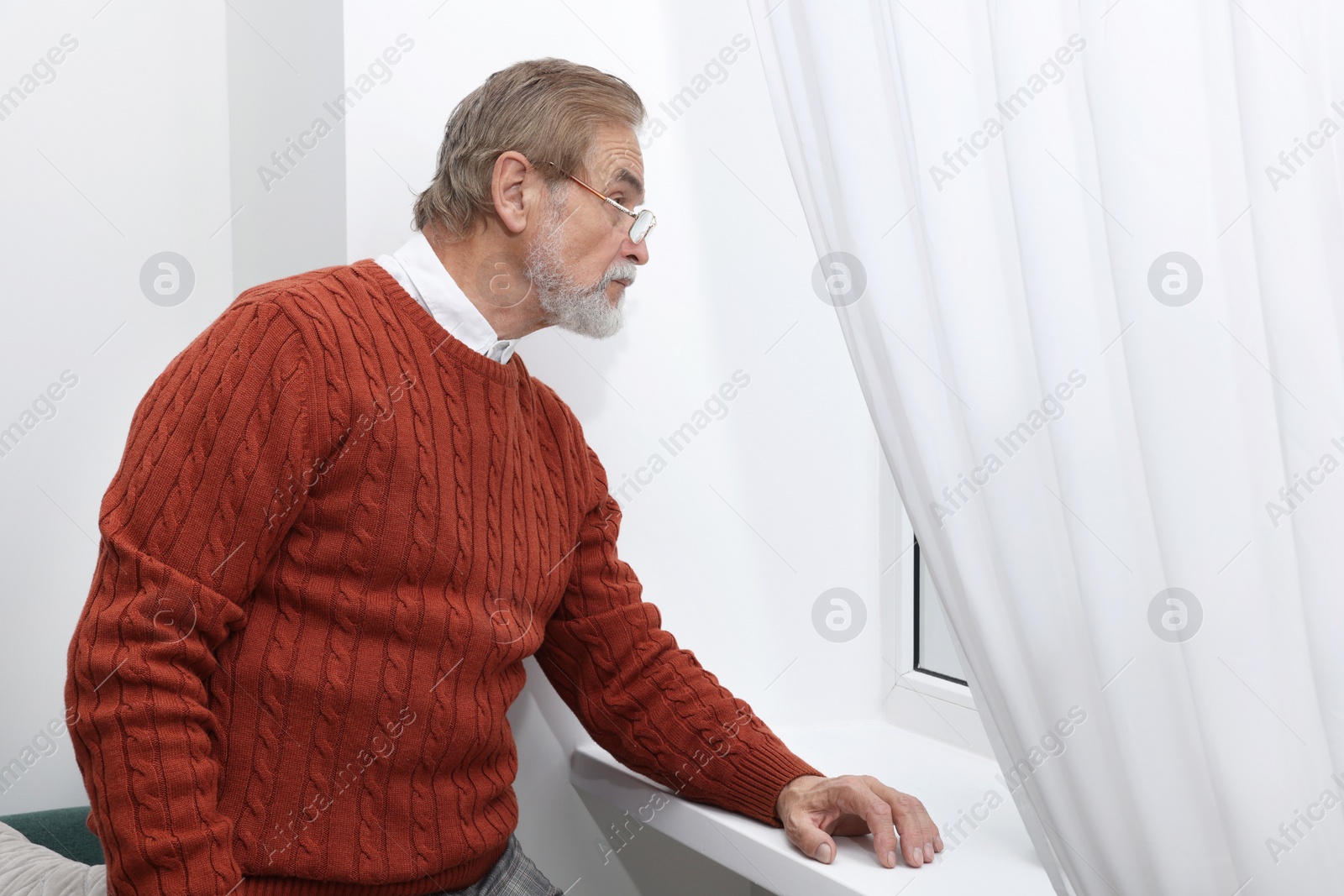 Photo of Upset senior man looking at window indoors. Loneliness concept