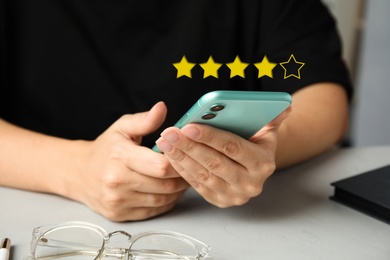 Image of Woman leaving review online via smartphone at table, closeup. Four out of five stars over gadget