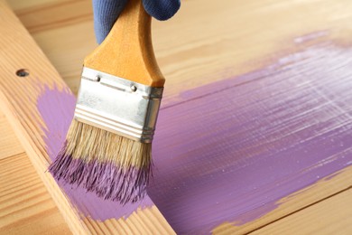 Photo of Worker applying violet paint onto wooden surface, closeup. Space for text