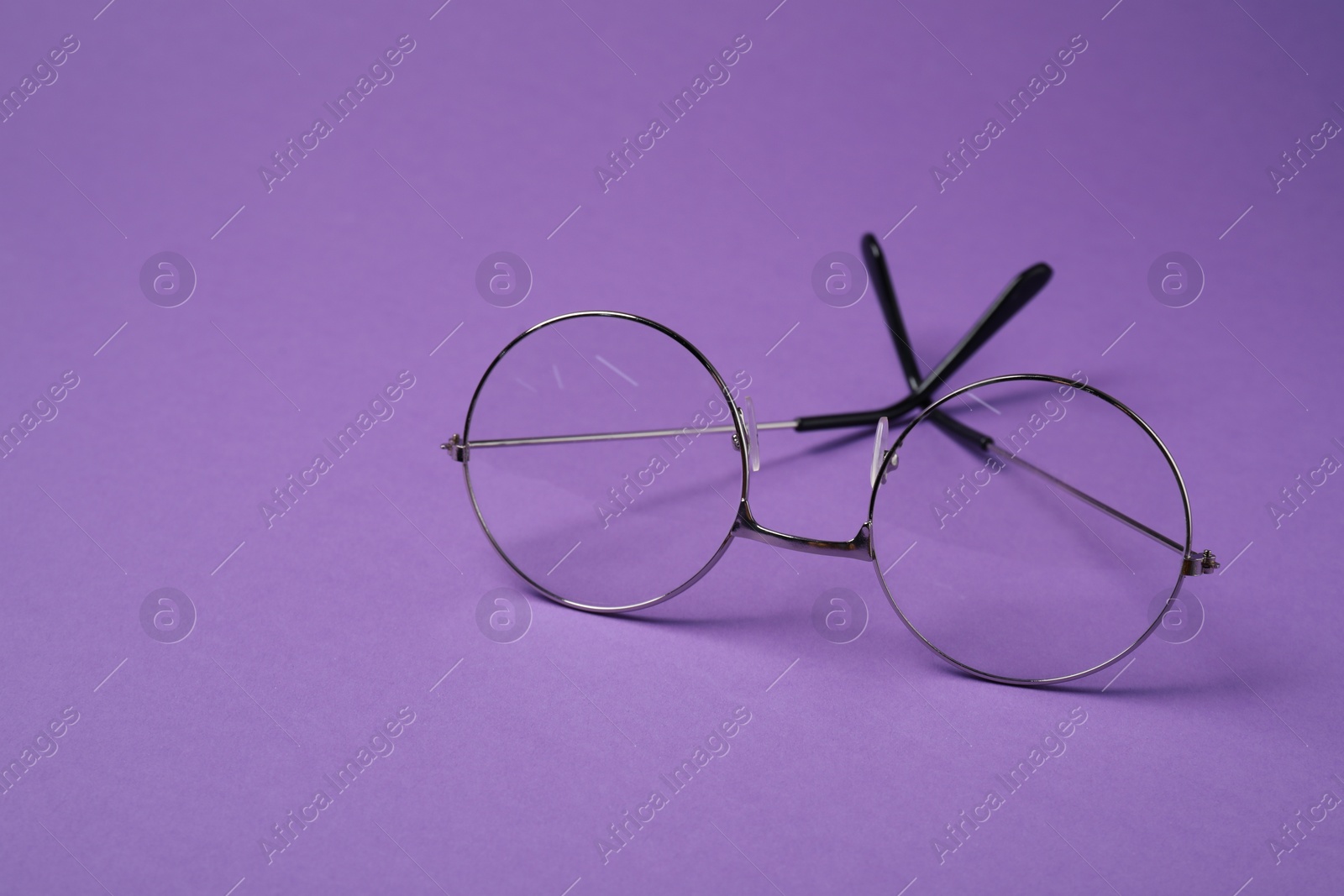 Photo of Stylish pair of glasses with metal frame on purple background. Space for text