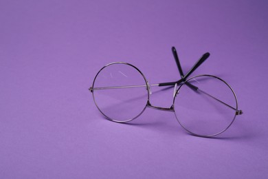 Stylish pair of glasses with metal frame on purple background. Space for text