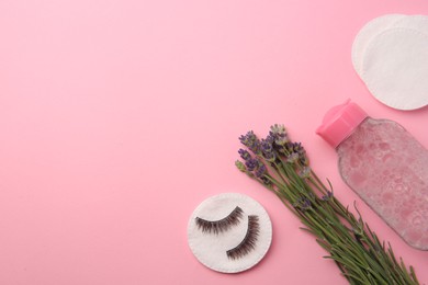Photo of Bottle of makeup remover, lavender, cotton pads and false eyelashes on pink background, flat lay. Space for text