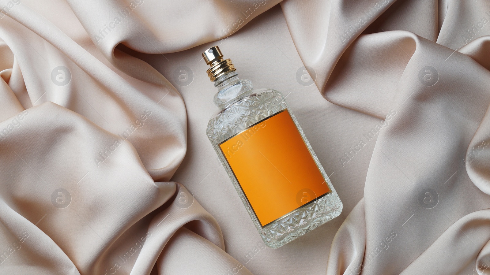 Photo of Luxury bottle of perfume on beige silk, top view